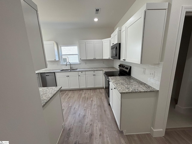 kitchen with dishwasher, light stone counters, black range with electric cooktop, white cabinetry, and a sink