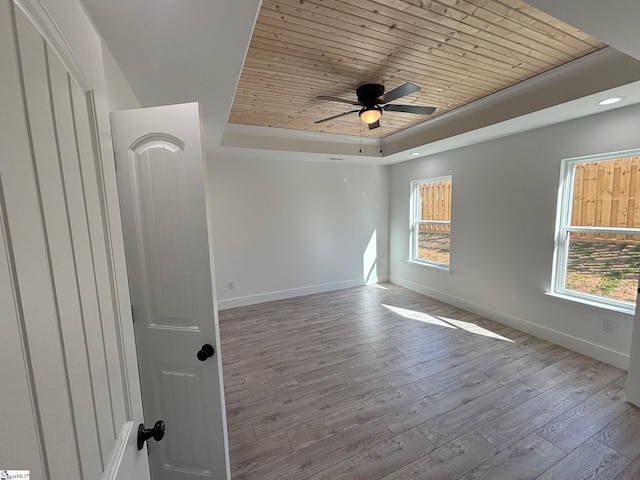 empty room with a wealth of natural light, a raised ceiling, wooden ceiling, and baseboards