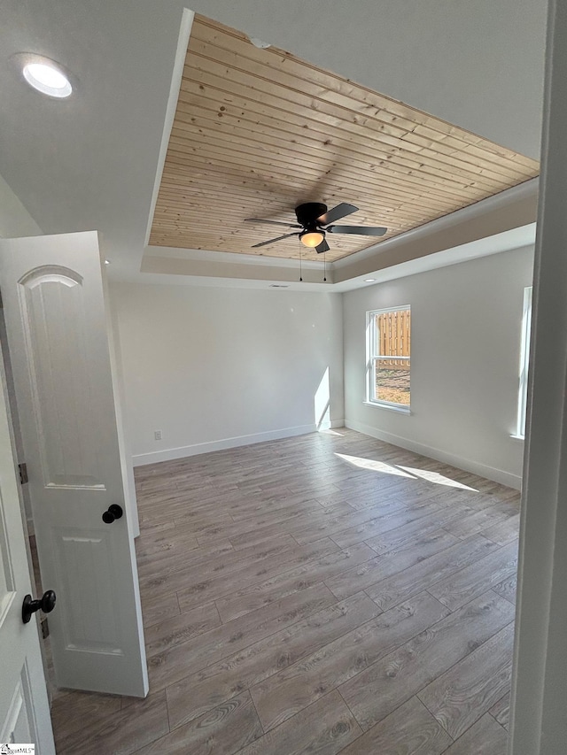 spare room featuring light wood-type flooring, wooden ceiling, baseboards, and a raised ceiling