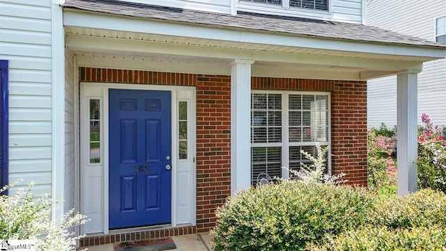 entrance to property featuring roof with shingles and brick siding