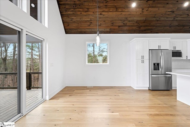 unfurnished dining area with high vaulted ceiling, light wood-style flooring, and baseboards