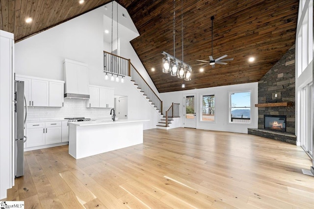 kitchen with light countertops, open floor plan, white cabinets, an island with sink, and wall chimney exhaust hood