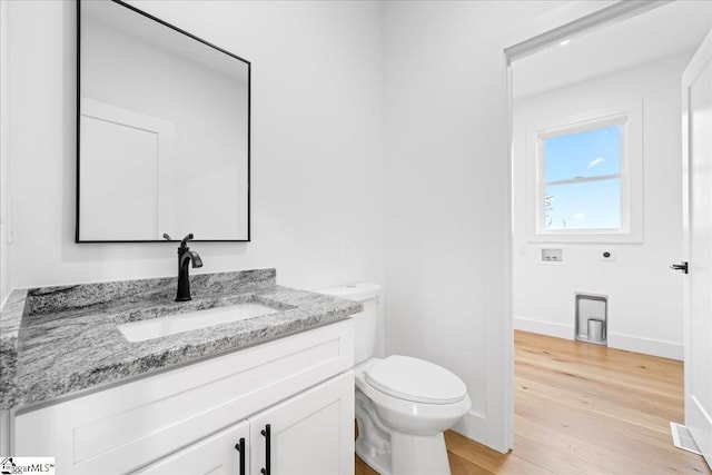 half bathroom featuring vanity, wood finished floors, toilet, and baseboards