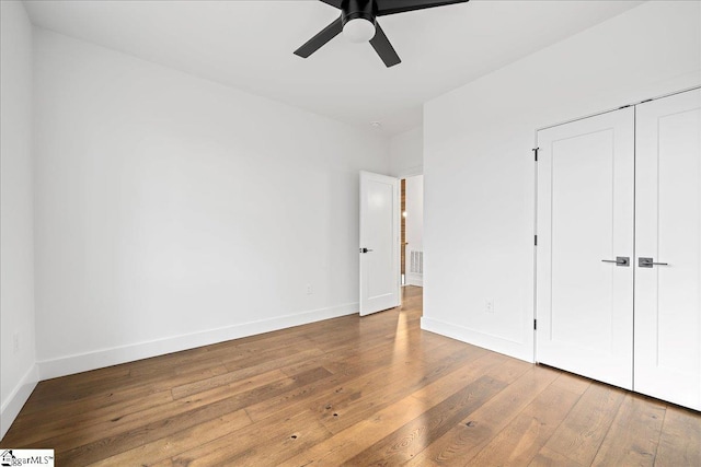 unfurnished bedroom featuring a closet, visible vents, a ceiling fan, wood finished floors, and baseboards