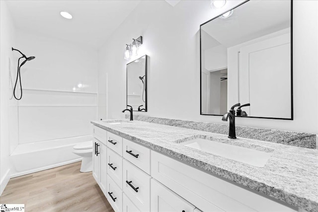 bathroom featuring double vanity, a sink, toilet, and wood finished floors