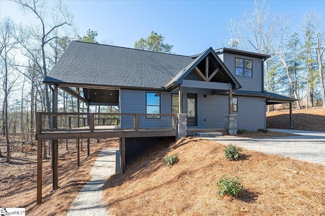 view of front of property featuring dirt driveway and a shingled roof