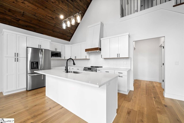 kitchen with light countertops, appliances with stainless steel finishes, white cabinets, a sink, and premium range hood