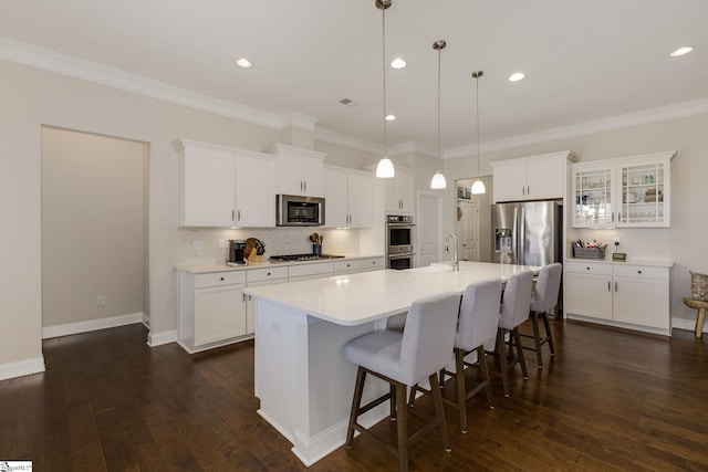 kitchen featuring decorative backsplash, appliances with stainless steel finishes, a breakfast bar, dark wood-style flooring, and a kitchen island with sink