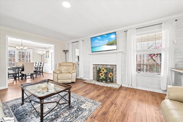 living area with a wealth of natural light, a fireplace, wood finished floors, and an inviting chandelier