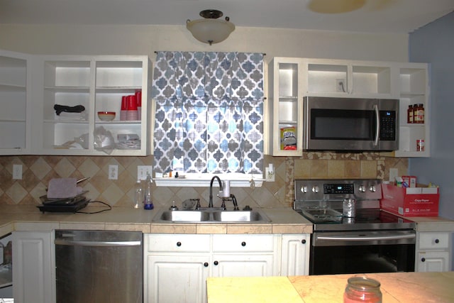 kitchen with light countertops, backsplash, appliances with stainless steel finishes, white cabinets, and a sink