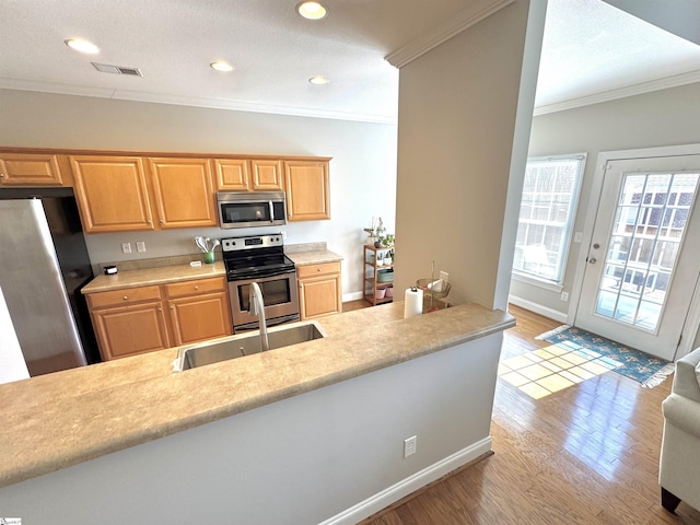 kitchen with stainless steel appliances, crown molding, light countertops, light wood-type flooring, and a sink