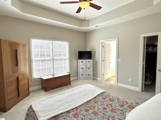 bedroom with baseboards, light colored carpet, ensuite bath, a spacious closet, and a tray ceiling