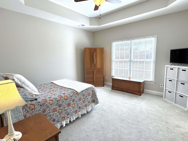 carpeted bedroom with baseboards, visible vents, a tray ceiling, and a ceiling fan