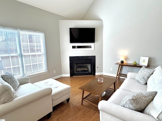 living area with vaulted ceiling, a tiled fireplace, wood finished floors, and baseboards