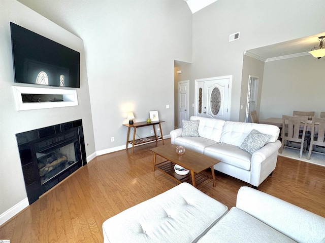 living area with baseboards, visible vents, ornamental molding, wood finished floors, and a fireplace