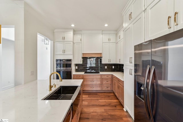 kitchen with light stone countertops, black appliances, white cabinetry, and a sink