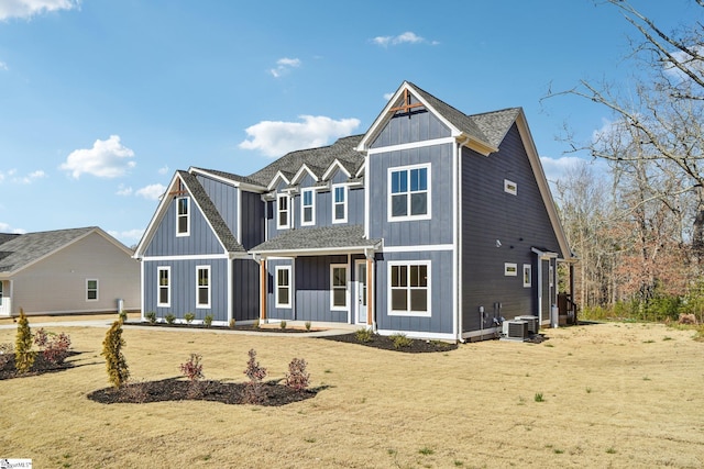 view of front of home with a shingled roof, central AC, board and batten siding, and a front yard