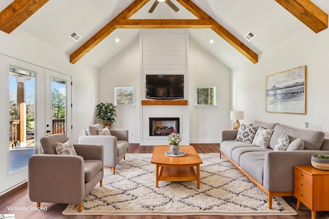 living room with a large fireplace, visible vents, beamed ceiling, and wood finished floors