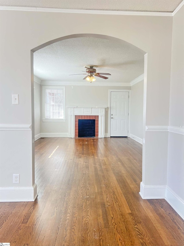 unfurnished living room with a textured ceiling, ceiling fan, ornamental molding, and wood finished floors