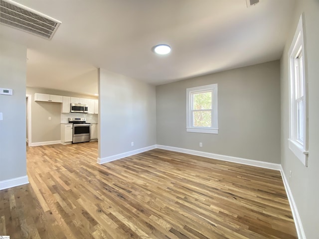 unfurnished room with light wood-type flooring, visible vents, and baseboards