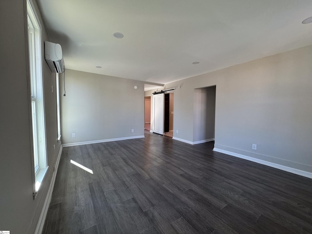 empty room with a barn door, baseboards, dark wood-style flooring, and a wall mounted air conditioner