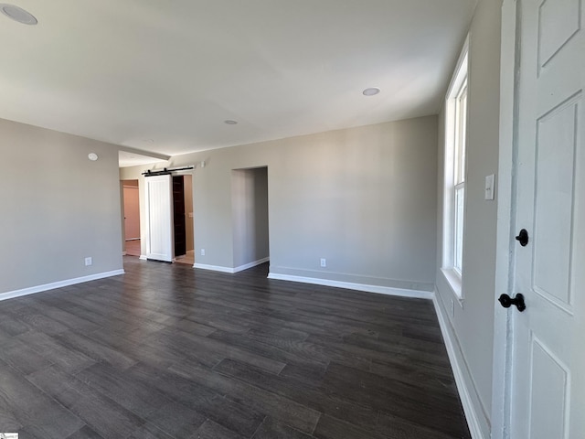 unfurnished room featuring a barn door, baseboards, and dark wood-type flooring