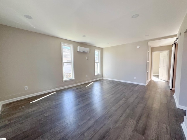 spare room with dark wood-style floors, a barn door, baseboards, and a wall mounted AC