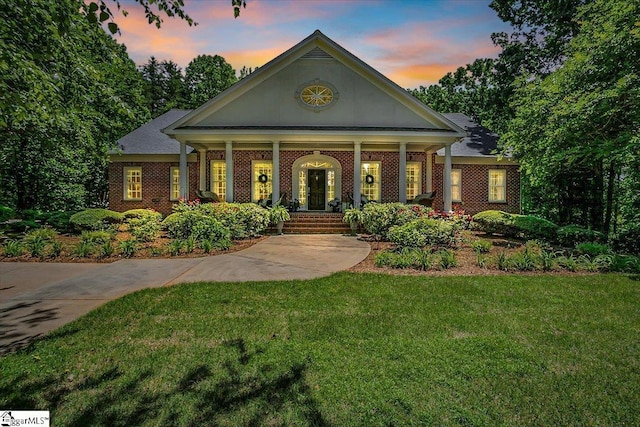 view of front of property featuring covered porch, brick siding, and a yard