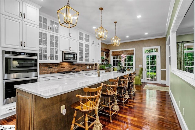 kitchen with white cabinets, a spacious island, glass insert cabinets, appliances with stainless steel finishes, and a kitchen breakfast bar