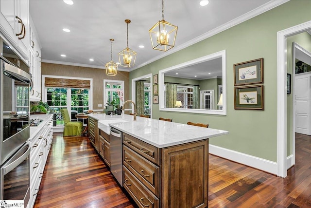 kitchen with decorative light fixtures, stainless steel appliances, white cabinets, an island with sink, and light stone countertops