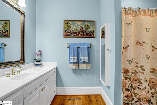 full bath with visible vents, vanity, baseboards, and wood finished floors