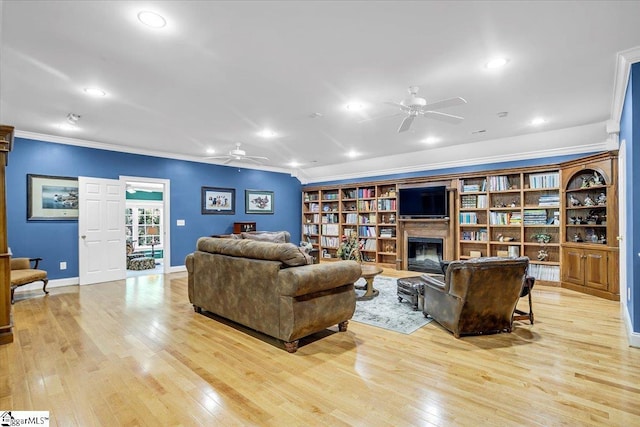 living area with light wood finished floors, ceiling fan, a fireplace, and ornamental molding