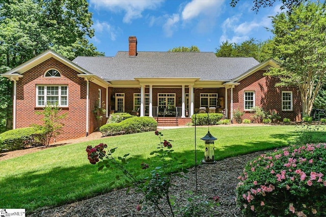 back of house with covered porch, brick siding, a yard, and a chimney