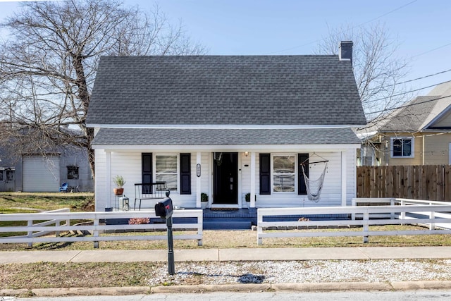 view of front of home with covered porch, roof with shingles, a chimney, and a fenced front yard