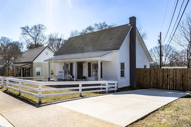 view of front facade featuring a porch, a shingled roof, a chimney, and a fenced front yard