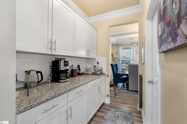 kitchen with tasteful backsplash, light stone countertops, ornamental molding, white cabinetry, and wood finished floors