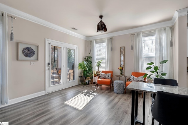 living area with baseboards, visible vents, ornamental molding, and wood finished floors