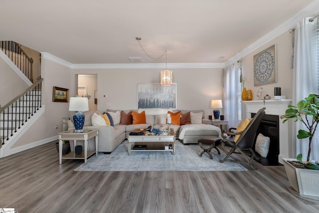 living room with baseboards, a fireplace with flush hearth, wood finished floors, stairs, and crown molding