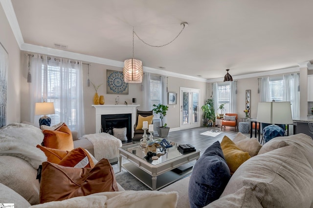 living room featuring ornamental molding, a glass covered fireplace, visible vents, and wood finished floors