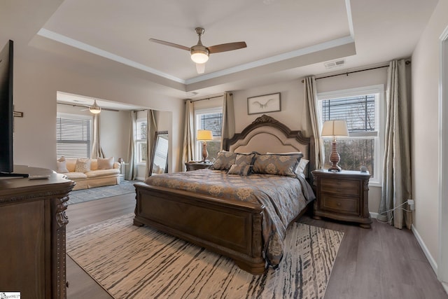 bedroom featuring a raised ceiling, multiple windows, and light wood-style flooring