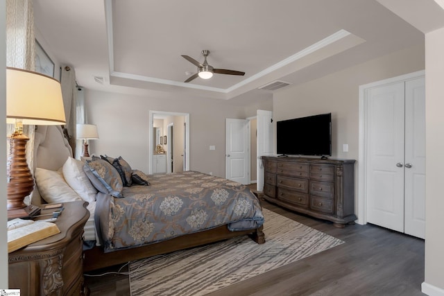 bedroom with ceiling fan, ensuite bathroom, dark wood-style flooring, visible vents, and a raised ceiling