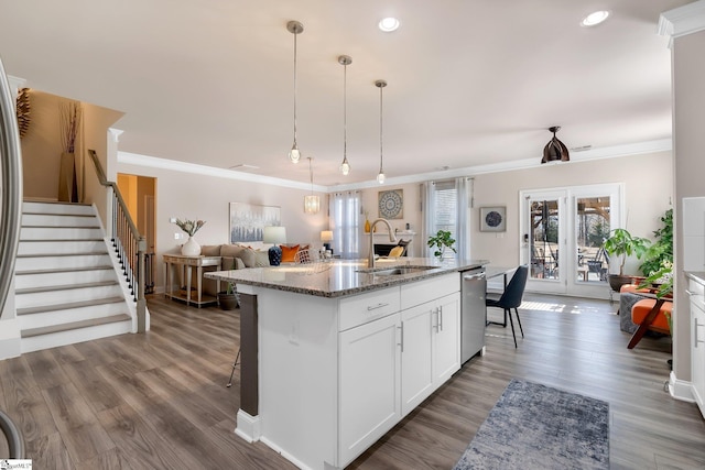 kitchen featuring an island with sink, dark stone countertops, stainless steel dishwasher, white cabinetry, and a sink