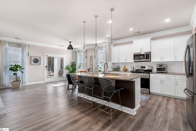 kitchen featuring white cabinets, appliances with stainless steel finishes, a kitchen island with sink, and pendant lighting