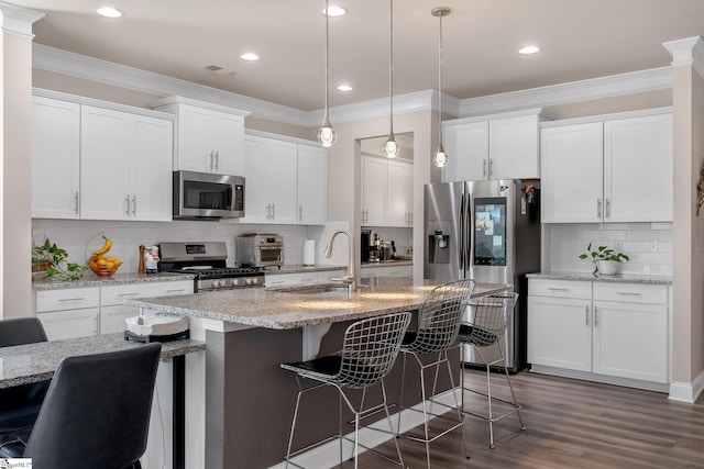 kitchen with decorative light fixtures, stainless steel appliances, a sink, white cabinetry, and a center island with sink