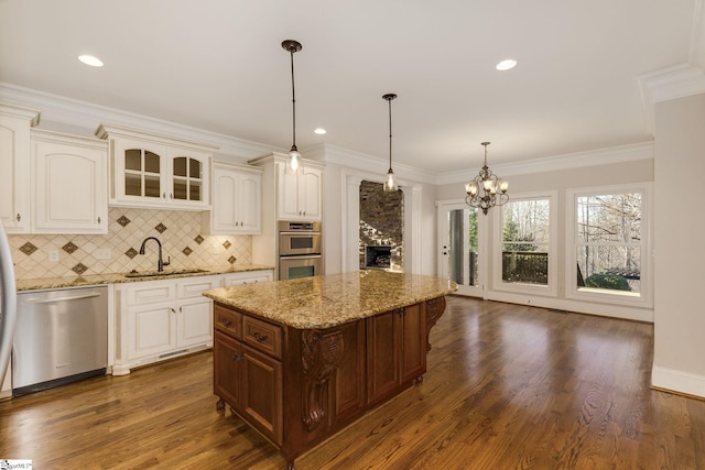 kitchen featuring light stone counters, pendant lighting, appliances with stainless steel finishes, glass insert cabinets, and a sink