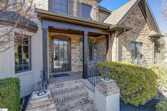 view of exterior entry with covered porch and roof with shingles