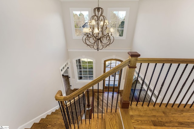 stairs with a chandelier, a towering ceiling, baseboards, and wood finished floors