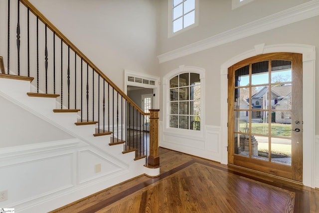 foyer entrance with a wainscoted wall, dark wood finished floors, a towering ceiling, and stairs