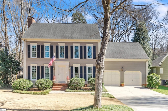 colonial home featuring a garage, concrete driveway, a chimney, and roof with shingles