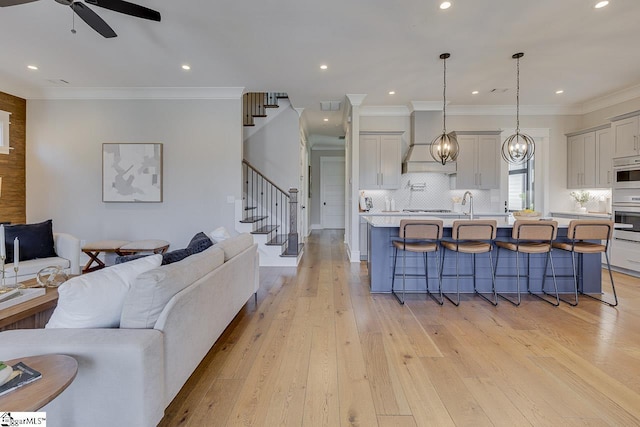 living room with a ceiling fan, stairway, crown molding, light wood-type flooring, and recessed lighting